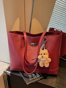 Retro burgundy tote bag with large capacity and decorative plush bear charm on a black desk