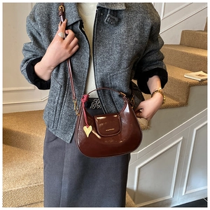 Detail of dark brown wax leather crescent bag with heart charm and woven strap