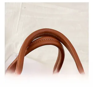 Detail of brown leather handbag with cylindrical handles and gold-tone hardware