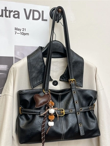 Retro black tote bag with white contrast stitching and decorative charms on a beige jacket