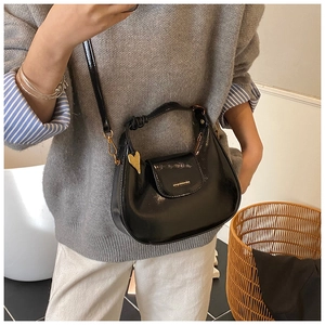 Detail of black patent leather half-moon bag featuring a gold heart charm and glossy finish