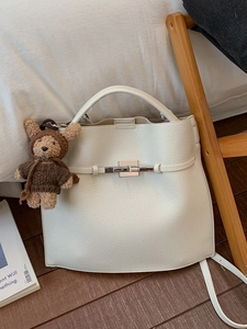 Cream lychee leather bucket handbag with silver buckle and bear charm in lifestyle setting
