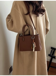 Sac à main marron à rayures verticales porté par un mannequin en manteau de laine beige