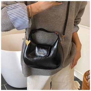 Detail of black patent leather hobo bag with golden heart pendant and metallic zipper