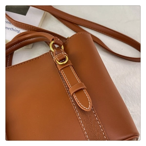 Detail of brown leather bucket bag featuring herringbone strap and gold hardware accents