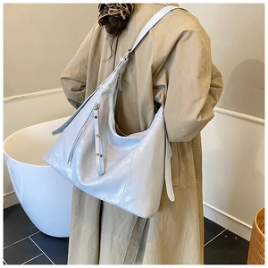 Détail d'un grand sac hobo bleu clair avec fermeture éclair porté avec un trench-coat chic
