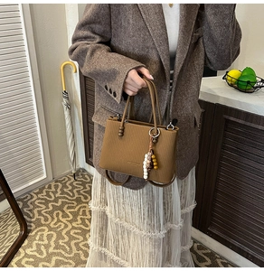 Sac bandoulière rétro marron avec texture à rayures verticales et breloque sur le modèle