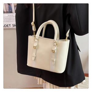 Detail of cream leather bucket bag showing dual handles and textured ribbon accent