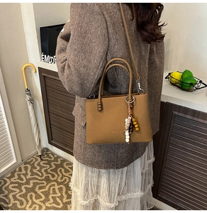 Close-up of brown textured mini tote bag with pleated patterns and beaded charm