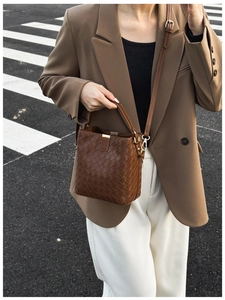 Détail du sac seau en cuir tressé marron foncé avec finitions dorées sur un mannequin