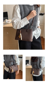 Detail of dark brown textured leather tote featuring a retro beaded charm and adjustable strap