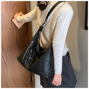 Détail d'un grand sac seau noir avec zip argenté et gland en cuir porté par un modèle