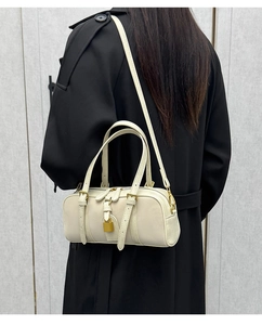 Detail of cream Boston bag with gold hardware worn over a long black winter coat