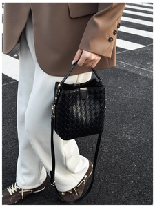 Détail du sac seau noir tressé avec finitions dorées et bandoulière réglable