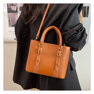 Detail of brown leather tote bag with white contrast stitching and gold metal hardware