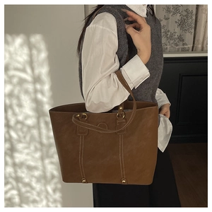 Detailansicht der braunen Leder-Einkaufstasche mit eleganten goldenen Beschlägen am Modell