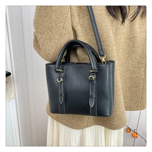Detail of black bucket bag with white stitching and gold hardware on model