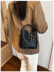 Détail du sac seau en cuir tressé noir avec garnitures dorées porté à l'épaule