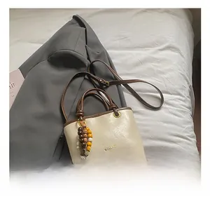 Detail of a beige crossbody bag with brown trim and ethnic beaded charm decoration