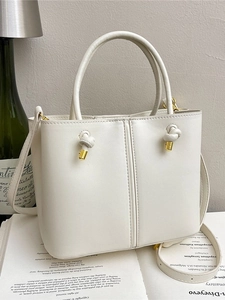 Elegante cremefarbene Beuteltasche mit Knotendetail und Schultergurt auf Buch
