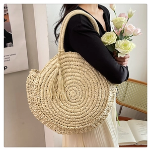 Detail of round beige woven straw bag with tassel charm and twin handles in a lifestyle setting