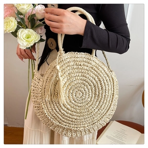 Detail of round beige woven straw bag with tassels and circular handles for beach travel