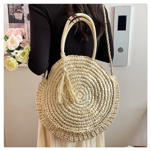 Detailed view of a large round straw bag with tassels and shoulder strap for vacation