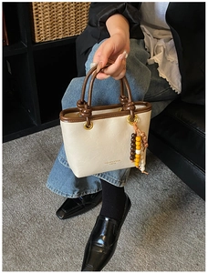 Detail of cream PU leather tote bag with brown handles and colorful beaded charm