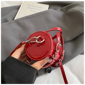 Detalle de mini bolso cilíndrico en charol rojo con herrajes plateados y acabado brillante
