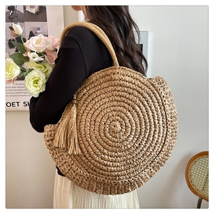 Detail of a large round woven straw bag with long tassels and a bohemian summer vibe
