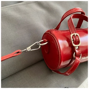 Detalle de mini bolso cilíndrico rojo con cierre plateado e inscripción blanca Hello