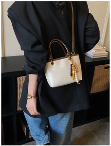 Detail of minimalist cream tote bag with brown handles and vintage colorful bead charm
