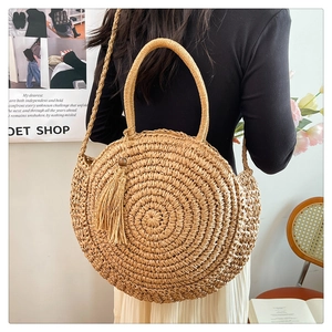 Detail of hand-woven straw shoulder bag featuring a round design and chic tassel charm