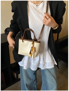 Detail of a beige crossbody bag with dark brown straps and a colorful beaded tassel charm