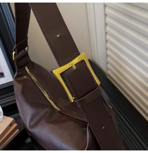 Detail of a dark brown leather tote bag with a bold golden square buckle and wide strap