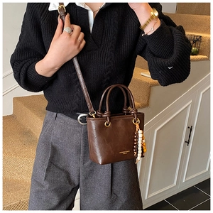 Detail of dark brown leather crossbody bag with beaded charm and gold text accent