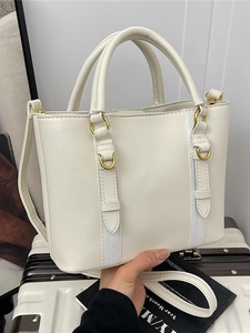 Chic beige leather bucket bag with top handle and shoulder strap on white suitcase