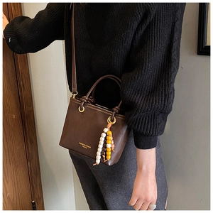 Detail of dark brown crossbody bag featuring matte leather texture and beaded pendant charm