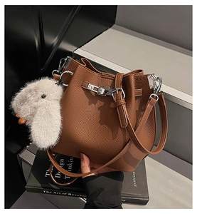 Detail of brown litchi pattern bucket bag with metal twist lock and plush bunny charm