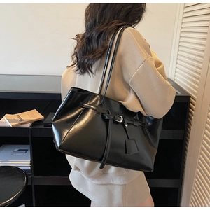 Detail of high-capacity black leather tote bag with metal buckle and decorative tag