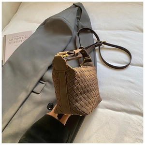 Detail of a brown woven leather crossbody bag with adjustable gold buckle on a white bed