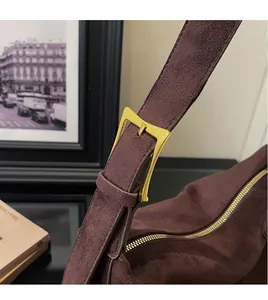 Detail einer dunkelbraunen Wildleder-Schultertasche mit breitem Gurt und goldener Schnalle