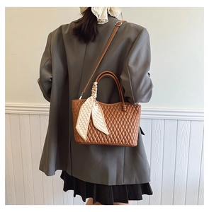 Close-up of brown quilted handbag with decorative silk scarf and adjustable strap
