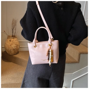 Detail of light pink PU leather bag featuring a tri-color wooden bead tassel and gold hardware