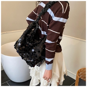 Detail of a black sequined tote bag with a metallic finish and ruffled shoulder strap
