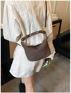 Close-up of dark brown woven leather crossbody bag with gold rivet strap details
