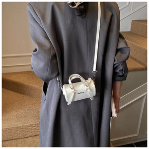 Bolso cilíndrico blanco cruzado sobre un atuendo minimalista en una escalera