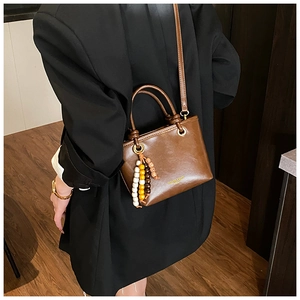 Detail of dark brown glossy leather crossbody bag with wooden bead charm on black blazer