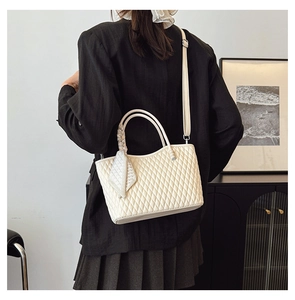 Detail of beige quilted tote bag with silk scarf handle worn by a model in minimalist interior