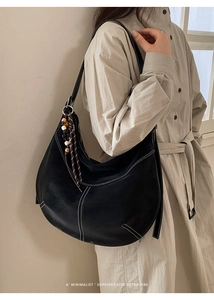 Détail du sac hobo en cuir noir avec surpiqûres blanches et pompon bohème